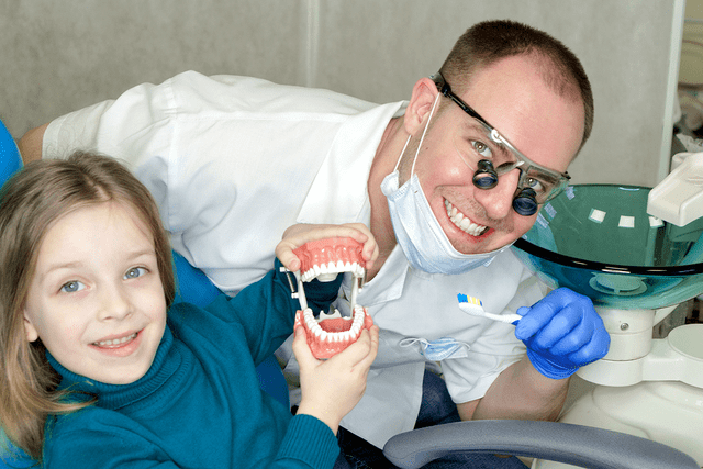 Left-handed dentist holding toothbrush poses with young patient