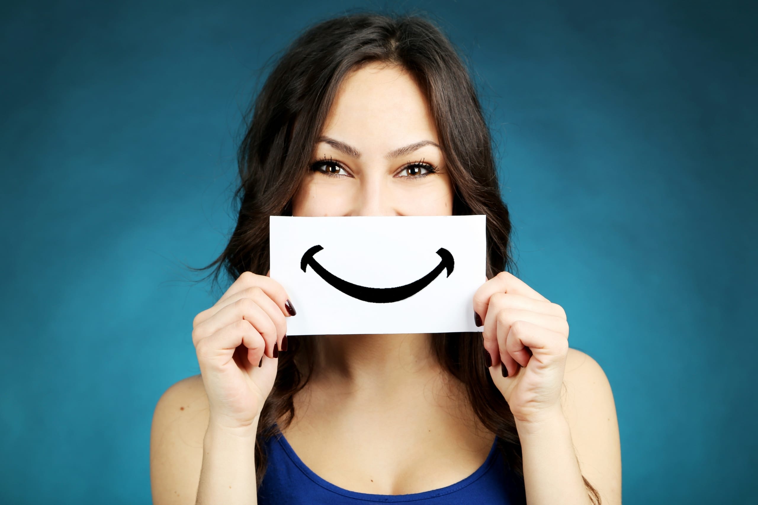 young woman holding paper smile in front of face, demonstrating the effect of positivity policies