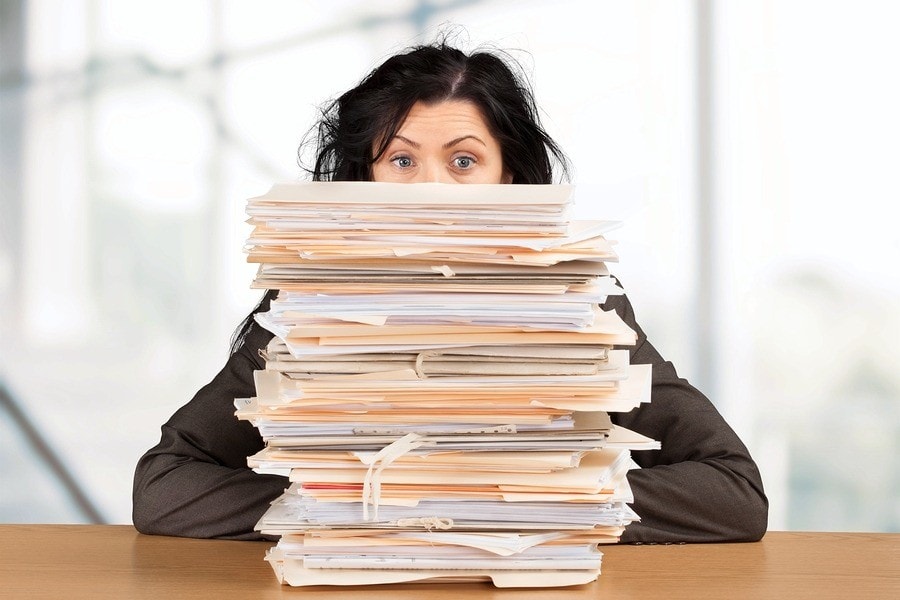 Large pile of paperwork in front of woman, illustrates that you should "play pack rat" with hiring documentation