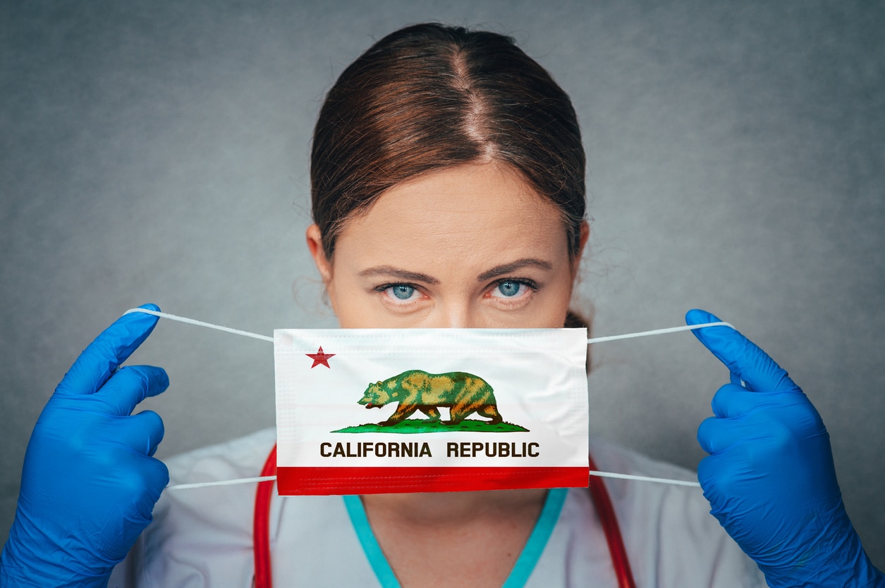 A female doctor puts on a COVID mask featuring the California State Flag; California's new covid laws